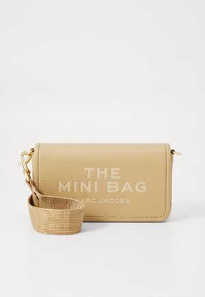 Mini borsa in pelle beige texture con pattina. Grande testo bianco "THE MINI BAG" e "MARC JACOBS" stampato sul davanti. Dotata di una tracolla intrecciata.