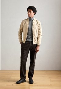 Beige bomber dzseki, szürke garbó, barna kordbársony nadrág és fekete sportcipő. Sima anyag, cipzáras zseb a dzseki karján.
