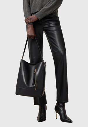 Czarna skórzana torba tote o luźnym fasonie, z przednią kieszenią na zamek, złotymi akcentami i minimalistycznym kształtem.