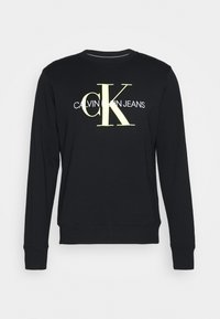 Černá mikina vyrobená z bavlny, s kulatým výstřihem, pružnými manžetami a lemem, s velkým žlutým logem "CK" a nápisem "CALVIN KLEIN JEANS".