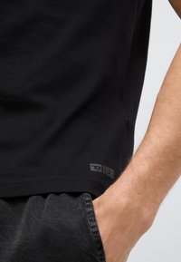 Μαύρο βαμβακερό T-shirt με λεία υφή, που διαθέτει μικρό γκρι λογότυπο Diesel στο τελείωμα και εφαρμόζει στενά γύρω από τ�ον κορμό.
