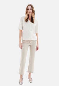 Hellbeige Kurzarm-Hemd mit Knöpfen, kombiniert mit hellbeige Cropped-Jeans und gemusterten High Heels. Das Outfit zeichnet sich durch eine lockere Passform und ein schlichtes Design aus.