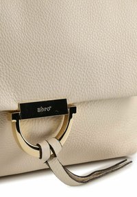 Borsa in pelle color crema con finitura testurizzata, dotata di chiusura metallica dorata e dettaglio decorativo con legatura in pelle.