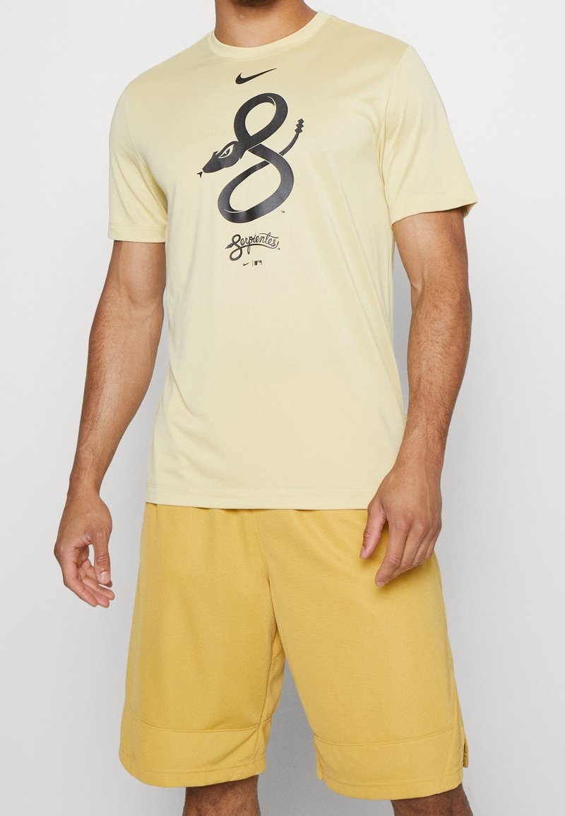 Camiseta de Nike de color amarillo con mangas cortas, que presenta un gráfico de una serpiente negra y texto. Combinada con pantalones cortos texturizados amarillos, tanto informales como atléticos.