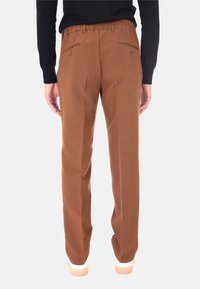 Persona che indossa pantaloni marroni a vita alta con tasche posteriori a bottone, un top nero a maniche lunghe e scarpe bianche, mostrata di spalle.