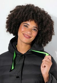 Chaqueta de plumas negra con capucha, que presenta tiras de acento en un brillante color verde y un acabado brillante. Tejido texturizado con un patrón de acolchado horizontal.