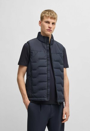 Die marineblaue Steppweste verfügt über einen hohen Kragen, einen Reißverschluss vorne und ein rechteckiges Steppmuster. Die glatte Textur und die seitlichen Taschen erhöhen die Funktionalität.
