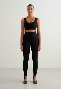 Svart aktivklädesset med en crop top med fyrkantig halsringning och högmidjade leggings. Slät, elastisk tyg med en figurnära silhuett och utskärningar vid anklarna.