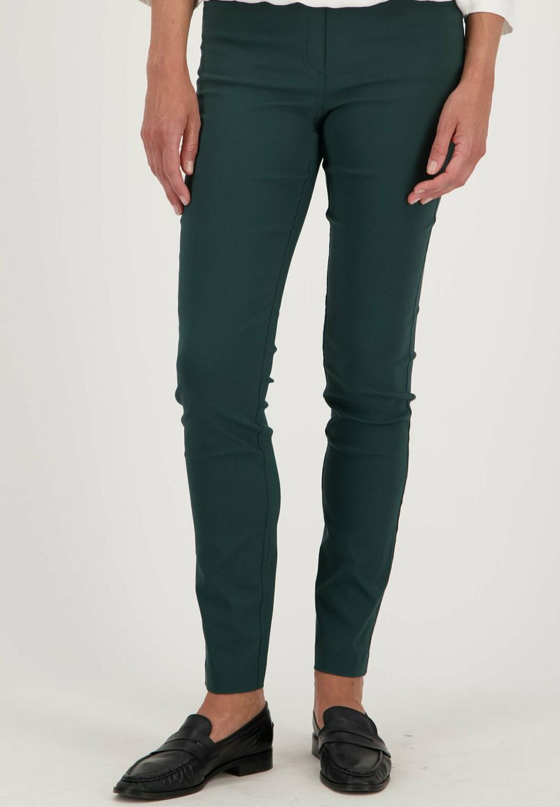 Donkergroene skinny pants van rekbare stof, met een gladde textuur en een eenvoudig ontwerp, gecombineerd met zwarte loafers.