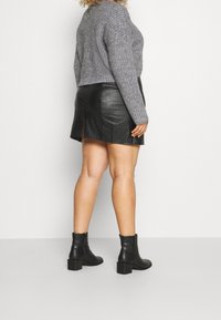 Szary sweter dzianinowy połączony z czarną skórzaną spódniczką mini z bocznym rozcięciem. Modelka nosi czarne botki za kostkę na słupkowym obcasie.