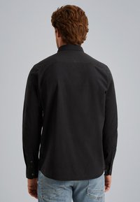 Una maglietta nera a maniche lunghe con colletto a bottoni, texture liscia e polsini abbottonati, abbinata a jeans blu chiaro.