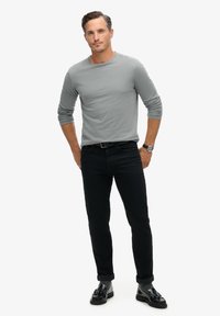 Grijze langemouwen shirt gecombineerd met zwarte slim-fit jeans en zwarte loafers, met opgerolde mouwen en een stijlvolle polshorloge.