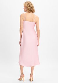Roze satijnen slipdress met smalle verstelbare bandjes, een rechte halslijn en een vloeiende midi-lengte zoom. De zachte textuur benadrukt de val ervan.
