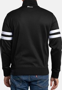 Chaqueta deportiva negra con cuello alto, franjas blancas en las mangas y puños acanalados. Presenta un pequeño logo "Roma" en el cuello.