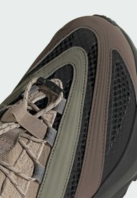 Chaussures à la conception robuste avec une surface texturée, accentuées en noir, marron foncé et vert olive, avec des détails en maille et des lacets.