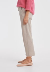 Pantalons beiges coupés avec des ourlets effilochés, associés à des chaussures plates roses. Le haut est un pull rose texturé, avec des manches trois-quarts.