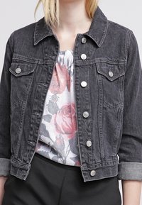 Czarna kurtka dżinsowa z kołnierzem, przednimi kieszeniami i srebrnymi guzikami. Posiada podwinięte rękawy i jest noszona na topie w kwiatowy nadruk.