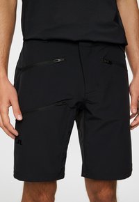 Svarta shorts tillverkade av ett mjukt, elastiskt tyg med flera fickor med dragkedja och en subtil logotypdetalj.