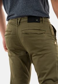 Pantalones chinos verde oliva con un diseño ajustado, que cuentan con dos bolsillos traseros y una cintura negra texturizada con un detalle de logotipo.