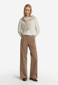 Ljusblå blus i mjukt material, kombinerad med beiga byxor med hög midja och vida ben. Bruna sandaletter med remmar kompletterar outfiten.