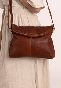 Braune Lederhandtasche mit lässigem Design, Reißverschluss und Schultergurt. Besitzt eine glatte Oberfläche und dezente Markenakzente.