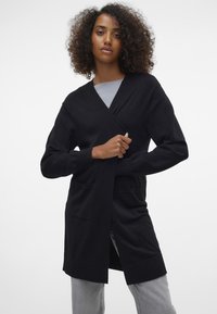 Zwarte cardigan met een wikkeldesign, lange mouwen en twee frontzakken. Gemaakt van zacht materiaal met een gladde textuur en een middenlange pasvorm.