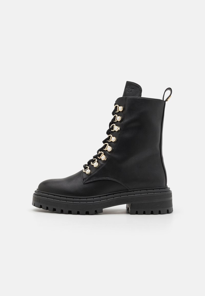 Botte de combat en cuir noir avec semelle épaisse, œillets dorés, lacets à l'avant et languette à l'arrière, vue de profil.