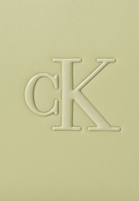 Pr präget beigem "cK"-logo på strukturert lys gul lærflate, sentrert og hevet for taktil detalj.