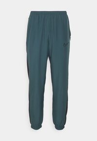 Tmavě tyrkysové jogger kalhoty s elastickým pasem, bočními kapsami a černými bočními detaily. Na přední straně se nachází malé černé logo Nike.