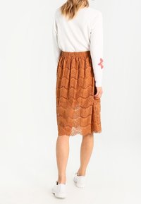 Brun blonde midi-skjørt med bølget mønster og elastisk talje, parret med en hvid sweater og hvide sneakers, der viser en afslappet pasform.