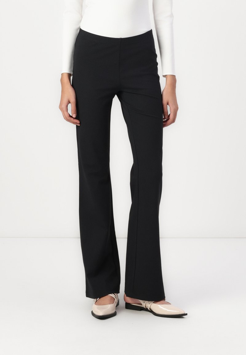 Pantalons évasés noirs avec une texture lisse et un matériau extensible, présentant une taille haute et un design minimaliste.