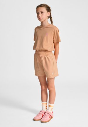 Ljusbrun jersey t-shirt med liten rosa logotyp, matchad med ljusbruna shorts med elastisk midja. Bärs med rosa sneakers och randiga strumpor.