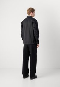 Black lightweight jacket with long sleeves, collared neckline, and loose fit, paired with black wide-leg trousers and black footwear.