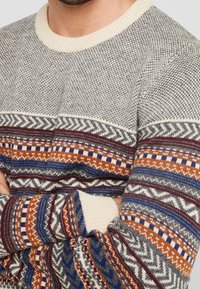 Gebreide trui met een gestructureerd grijs lichaam en mouwen met een multikleurig patroon in oranje, blauw en bordeauxrood accenten. Ribbelboord aan de halslijn en mouwen.