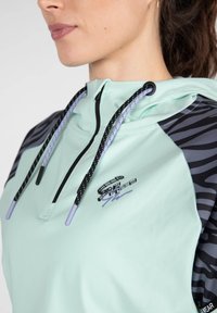 Sudadera verde menta clara con acentos de estampado animal en negro y gris, cordones ajustables con puntas moradas y un pequeño logo en la parte delantera.