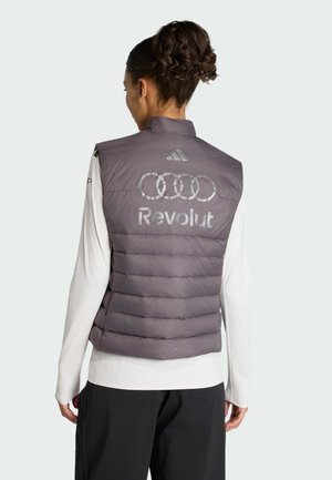 Kvinde set bagfra iført en grå polstret vest med Audi-ringe, Revolut-tekst og Adidas-logo over en hvid langærmet skjorte og sorte bukser.