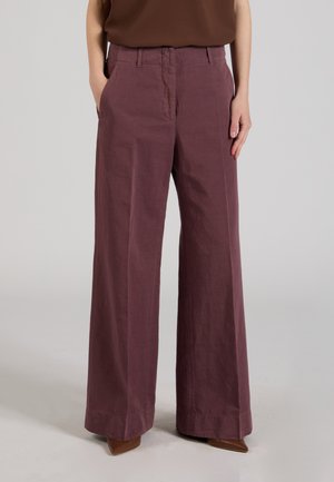 Pantaloni a gamba larga di colore prugna smorzato indossati con le mani nelle tasche e scarpe marroni appuntite, mostrati dalla vita al pavimento su sfondo neutro.