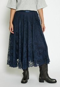 Gonna midi in pizzo blu navy con intricati motivi floreali, design svasato e una vita larga, abbinata a stivali neri fino al ginocchio.