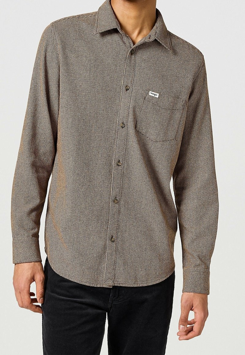 Brązowo-biała koszula w kratę z długim rękawem, kołnierzykiem na guziki i kieszenią z przodu, wykonana z lekkiego materiału. Na kieszeni widoczne charakterystyczne logo.