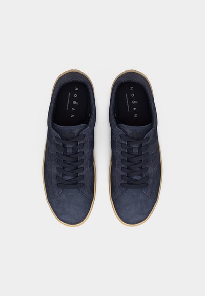 Paire de baskets en daim bleu foncé avec lacets noirs, semelles beige et marquage "Hogan" sur les semelles intérieures, vues de dessus sur un fond blanc.