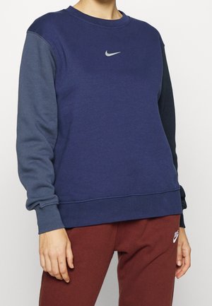 Granatowy sweter z szarymi rękawami, okrągłym dekoltem i małym, odblaskowym logo Nike na piersi; miły w dotyku materiał bawełniany.