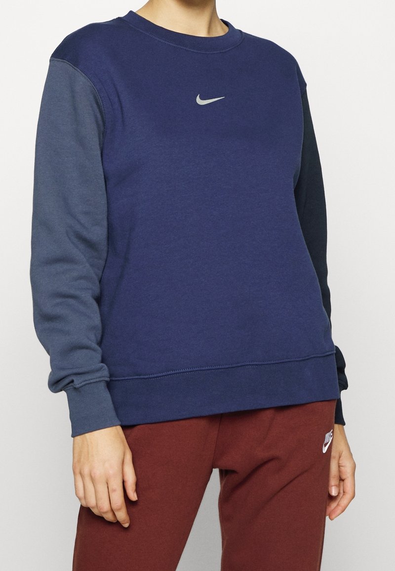 Mörkblå sweatshirt med grå ärmar, rund halsringning och en liten reflekterande Nike-logotyp på bröstet; mjukt bomullsmaterial.