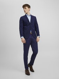 Mörkblå kostym med tvåknapplåt och slimfit-byxor, i kombination med en ljusblå skjorta och bruna snörskor, med skräddarsydd design.