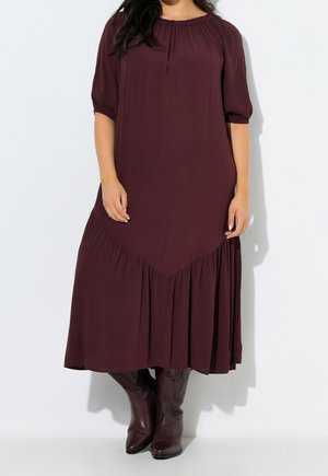 Femme portant une robe midi fluide bordeaux foncé avec des manches trois-quarts et des bottes de cow-boy bordeaux assorties.
