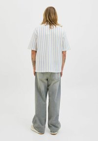 Chemise à manches courtes rayée en blanc avec des lignes bleues et grises, associée à un jean large gris clair. Design simple et décontracté.