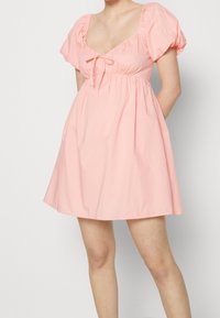 Vestido de algodón rosa con mangas abullonadas, corsé ajustado y un detalle de lazo en el pecho. La falda es acampanada, creando una silueta relajada.