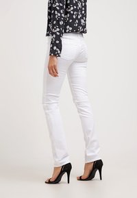 Jeans de mezclilla blanca con un diseño de pierna recta, que cuentan con dos bolsillos traseros y una textura suave, combinados con sandalias negras de tacón alto.