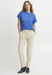 Top blu a maniche corte abbinato a pantaloni beige con due bottoni e tasche laterali. Stivali neri con tacco completano l'outfit.