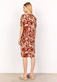Floral-patterned dress with a beige base, featuring bold rust red flowers, short sleeves, and a loose fit, paired with tan espadrille sandals.