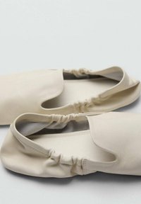 Beżowe miękkie baleriny ze skóry z elastycznymi otworami, zaokrąglonymi krawędziami i gładką teksturą; bez widocznych elementów metalowych ani wzorów.